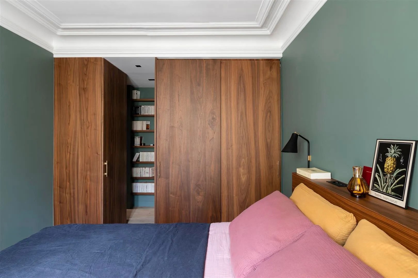 Chambre avec murs vert foncé, aménagements sur mesure en bois noyer et linge de lit coloré