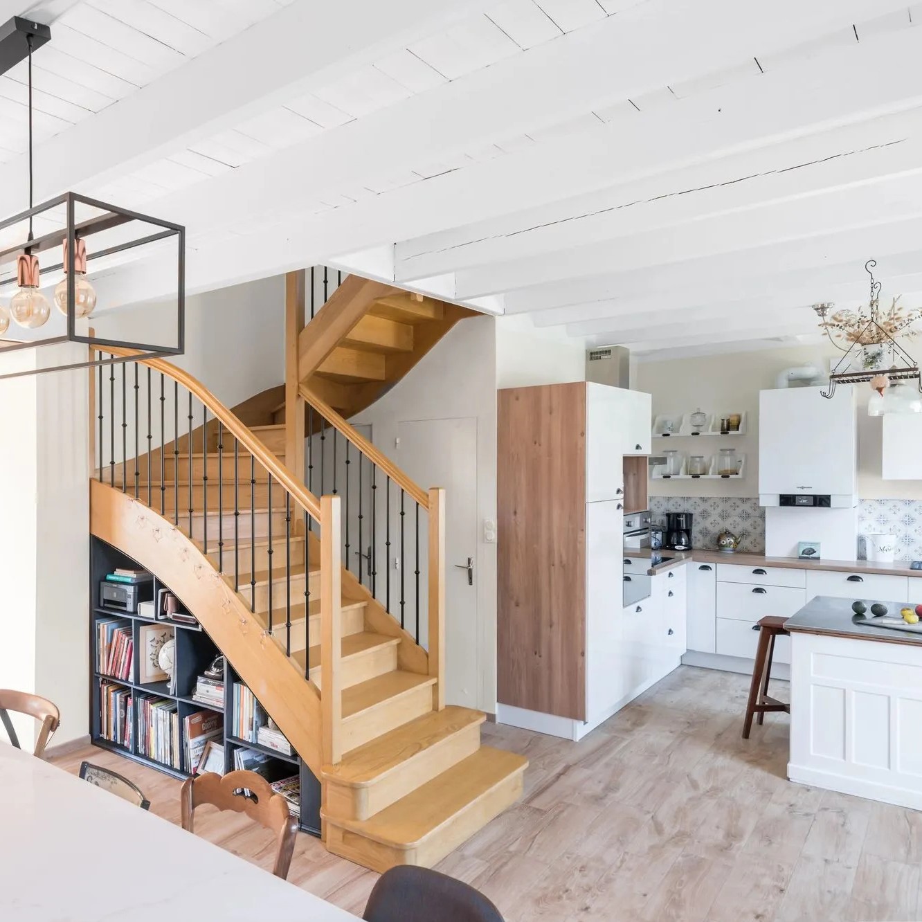 Escalier en bois central autour duquel gravitent cuisine, salle à manger et salon