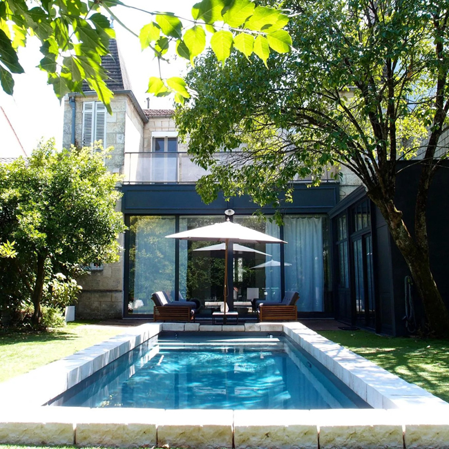 Une petite piscine dans un petit jardin de ville avec vue sur une maison ancienne