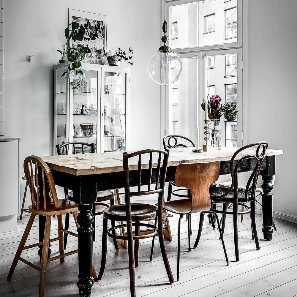 Chaises chinées autour de la table à manger, suspension en verre, vitrine en métal et verre