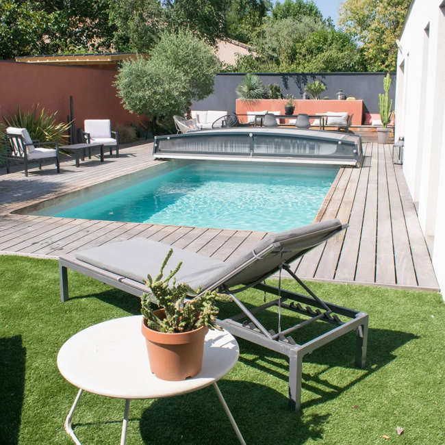 Un jardin avec terrasse en bois, piscine creusée et gazon synthétique